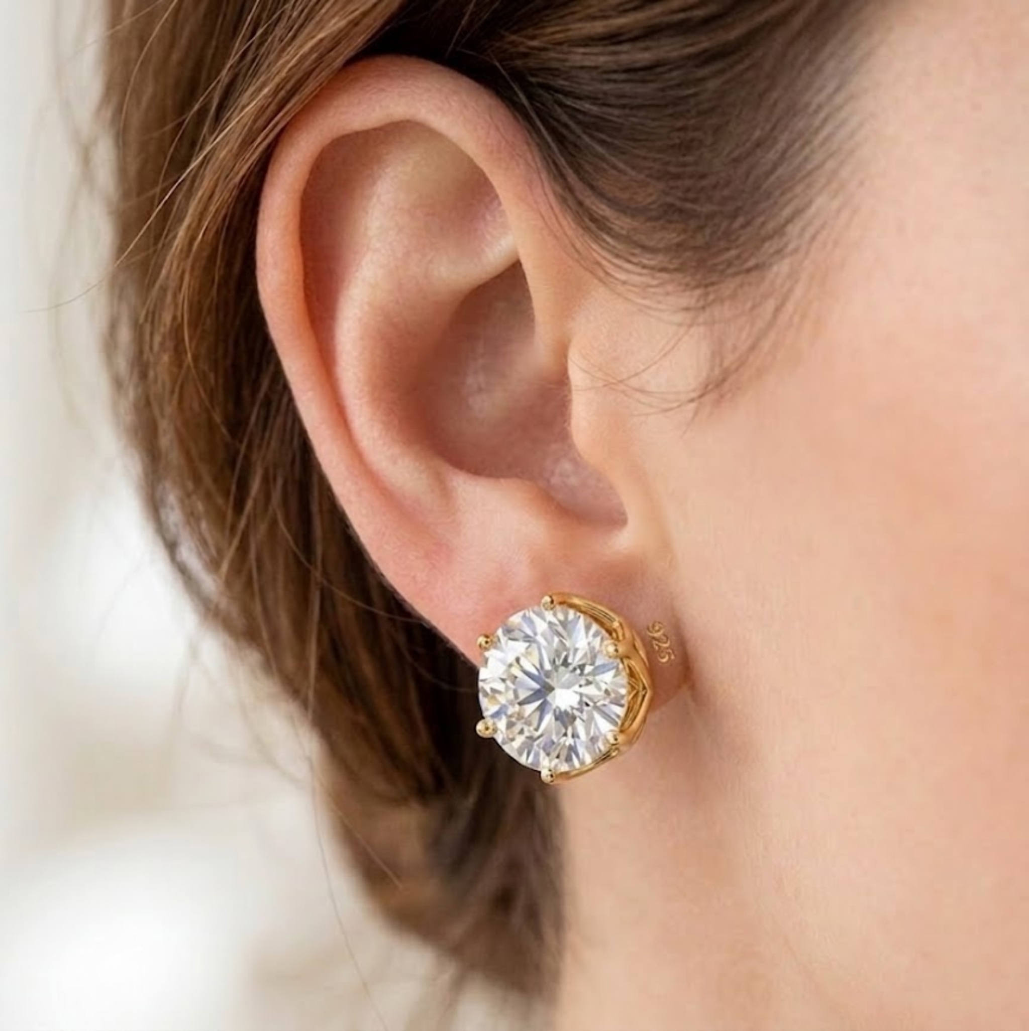 Gold earring worn on a person's ear with a blurred background lab grown diamond in Hyderabad